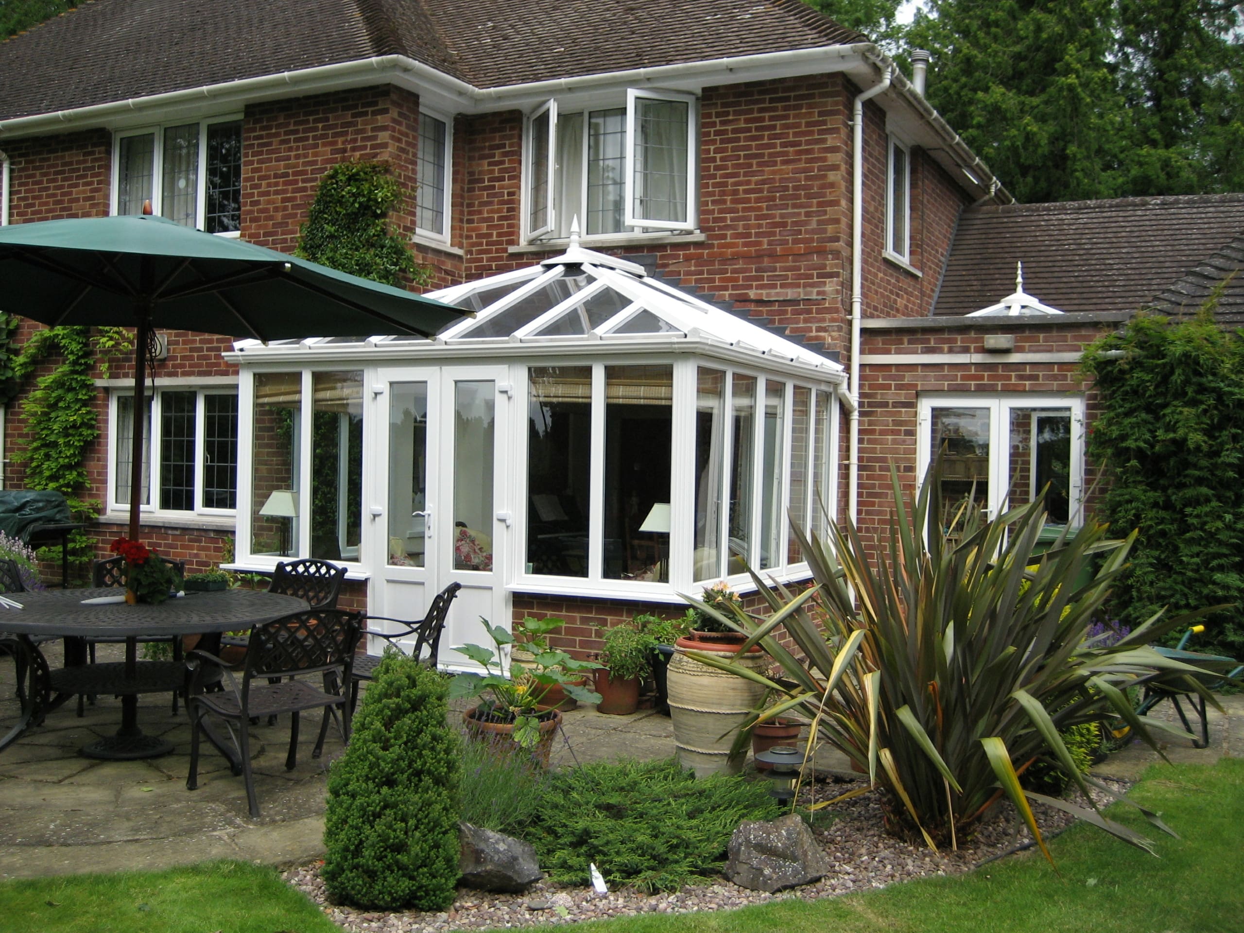 Rear of a property featuring mature shrubs and conservatory.