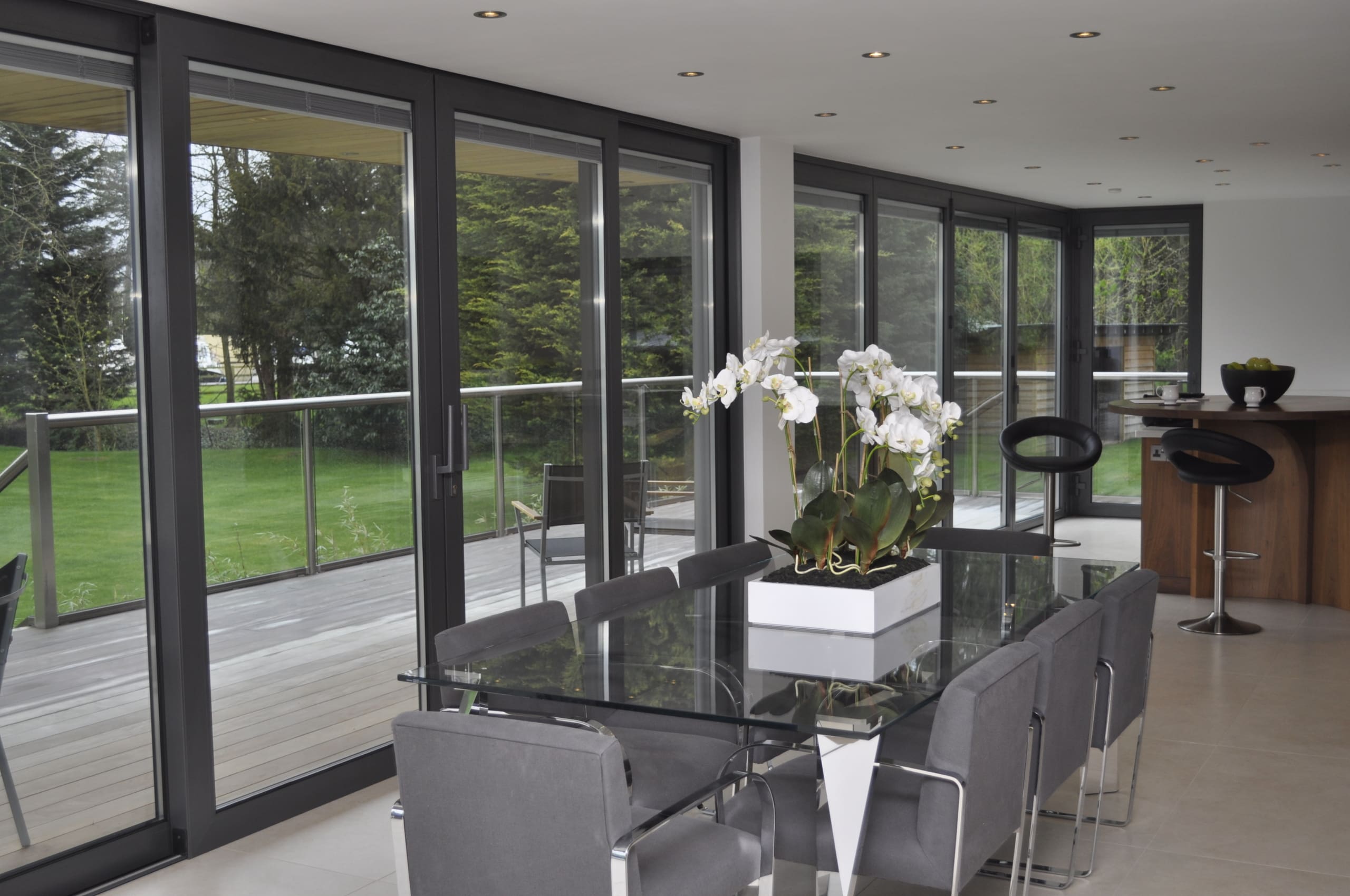 Modern home with glass table and grey chairs with orchards forming the centerpeice and grey bifolding doors providing views to the garden.