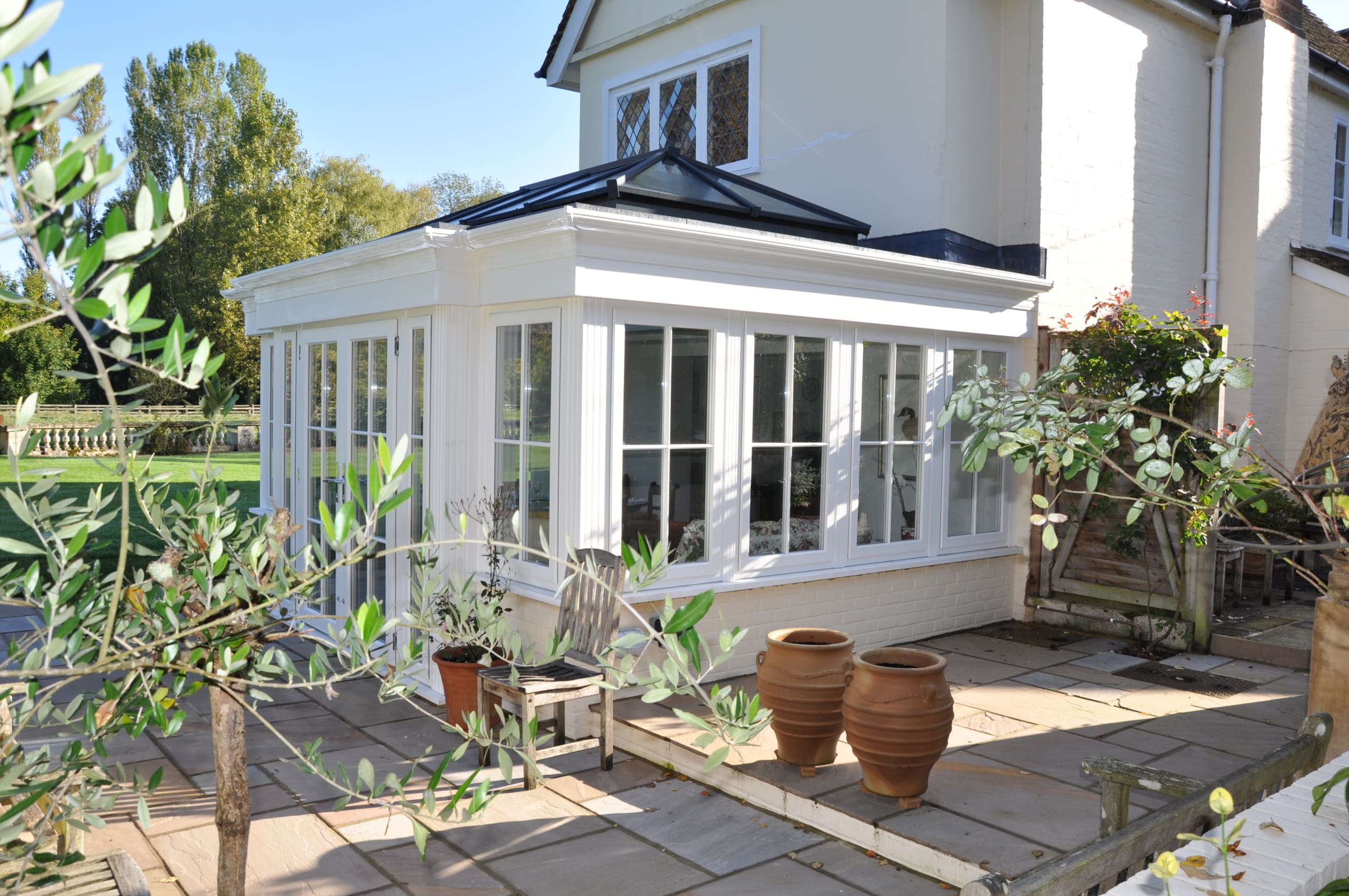 Exterior of a stunning orangery with roof lantern and mature garden plants.
