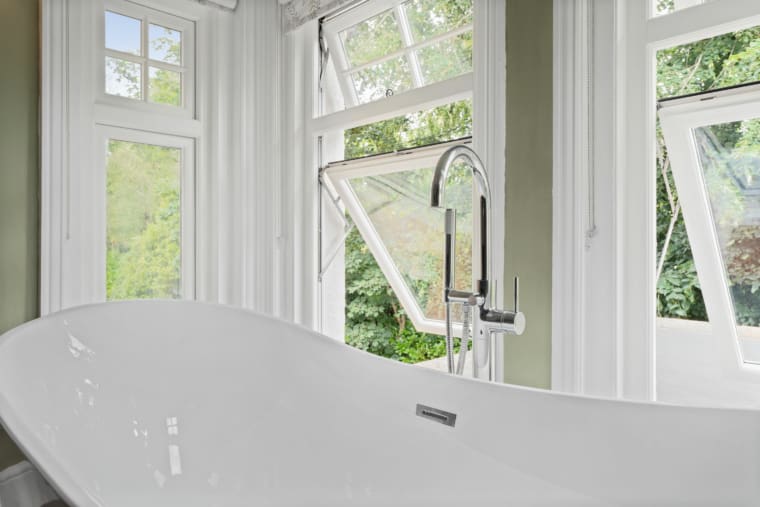 Bathroom windows surrounding a freestanding bath with mixer tap.