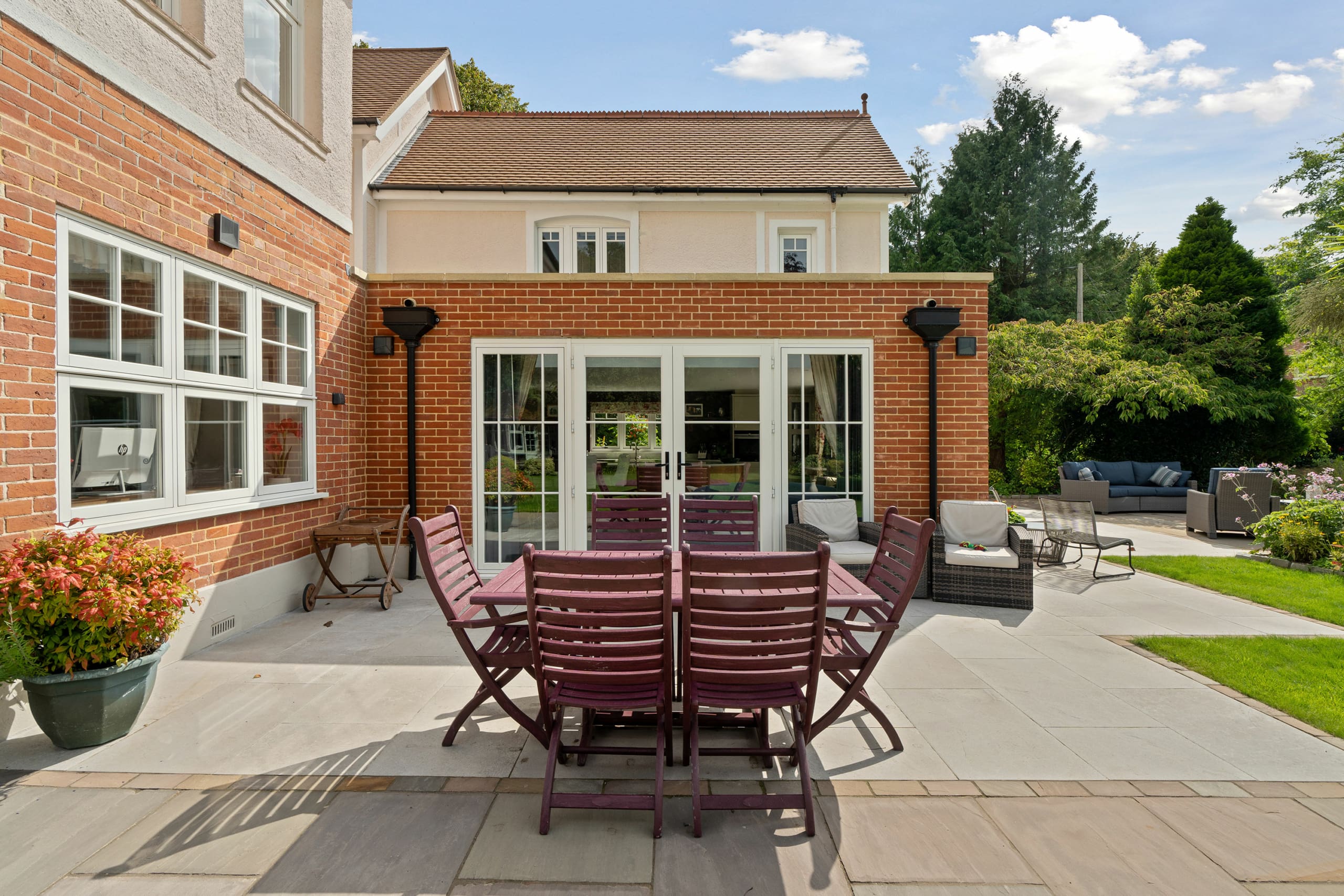 Substantial home with view of the modern brick extension with white french entrance doors and wooden garden furniture.