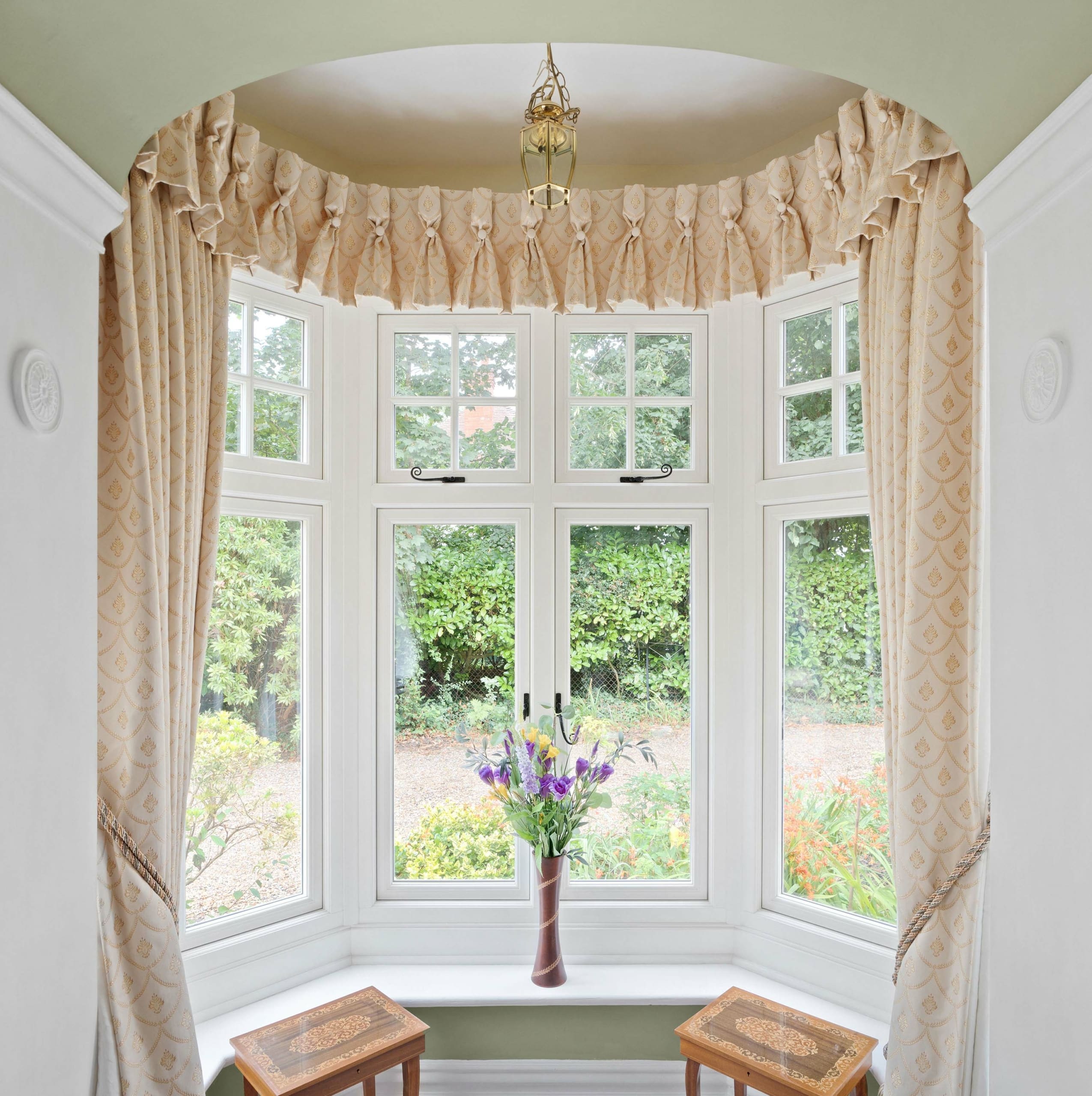 Bay window with traditional printed curtains, flowers and matching side tables.