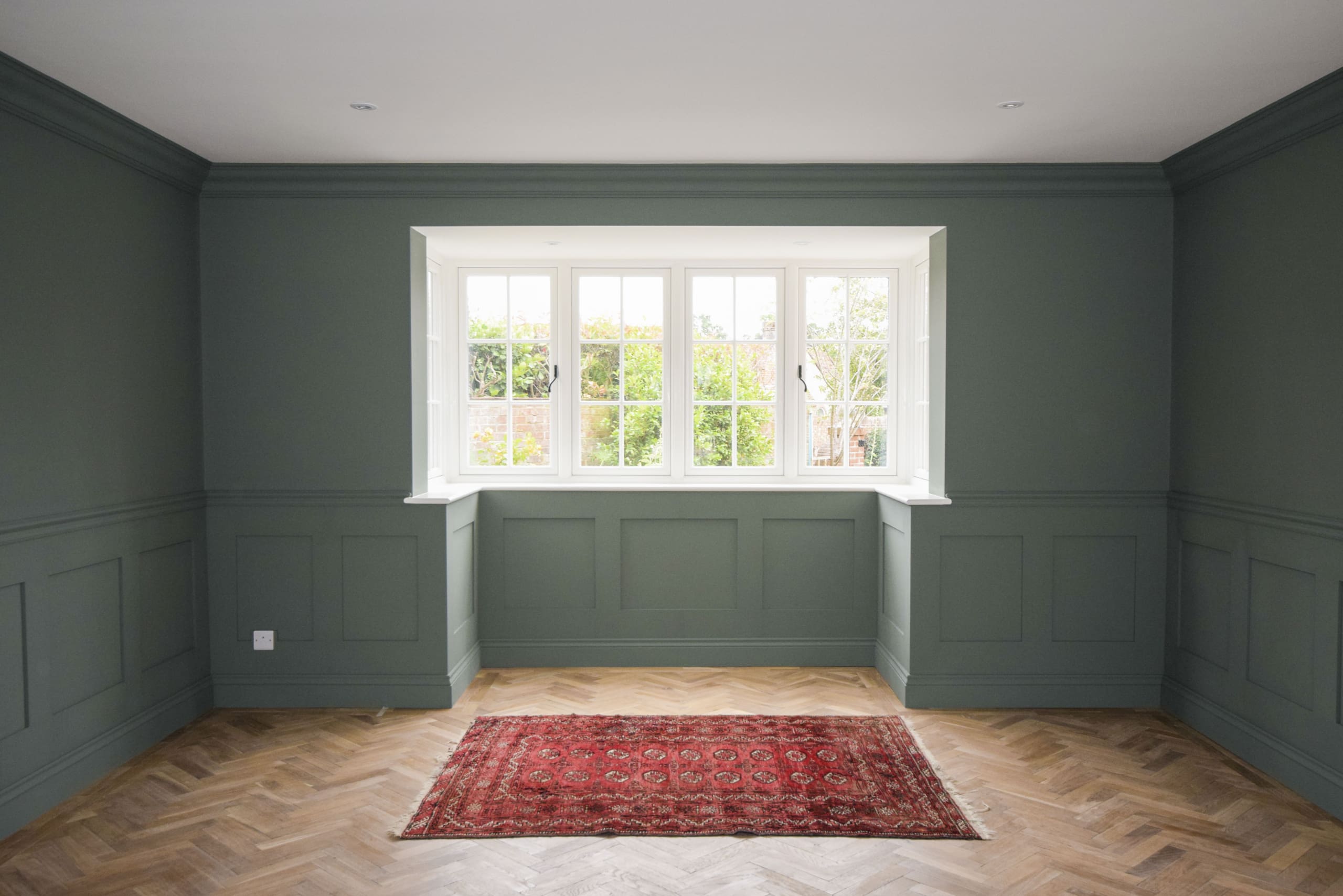 Living room with parquet flooring and aztec rug, bay window with traditional windows and dark green paintwork to the walls.