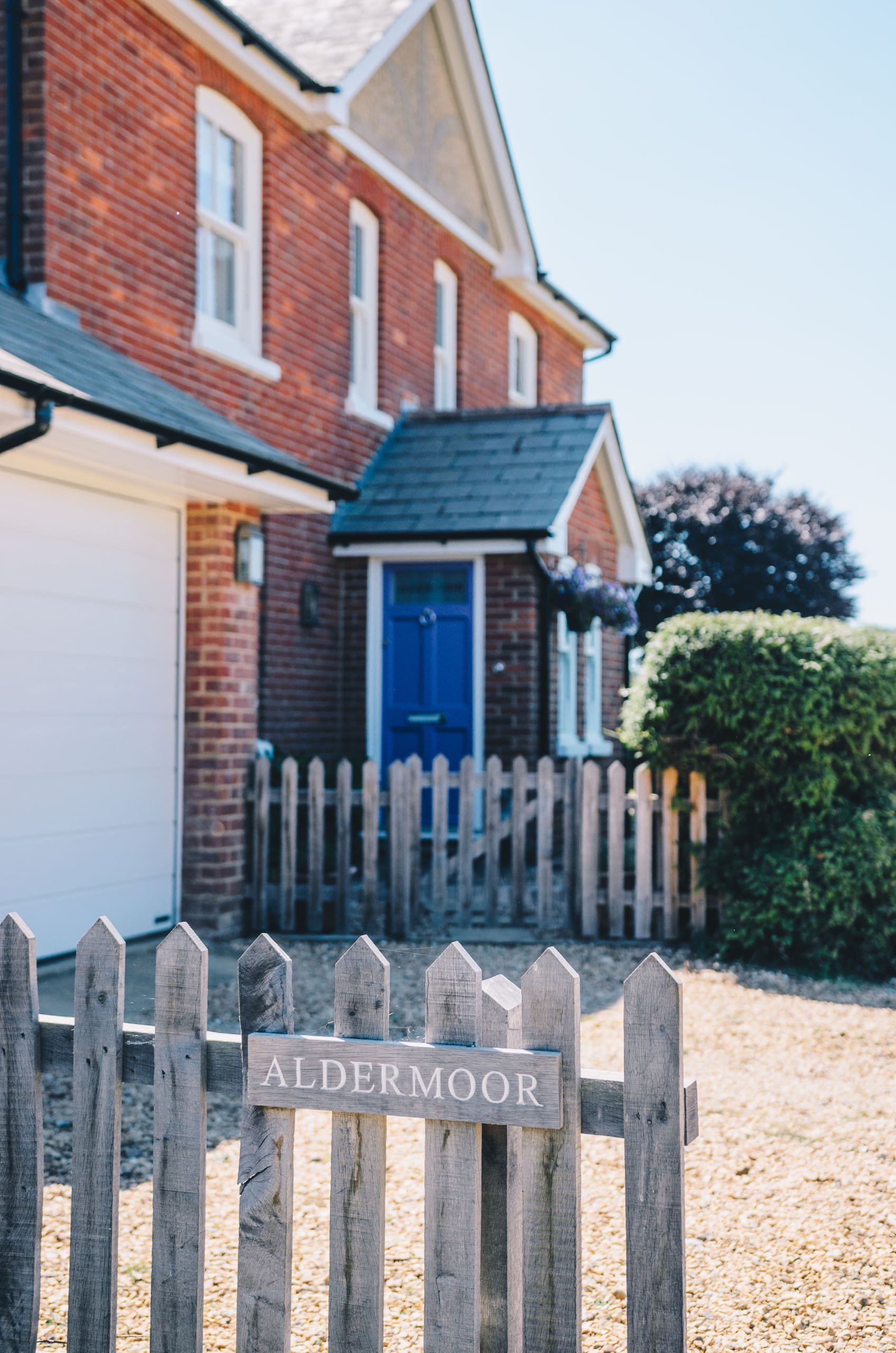 Exterior of a lovely home with the property name Aldermoor fixed in wood to a fence.