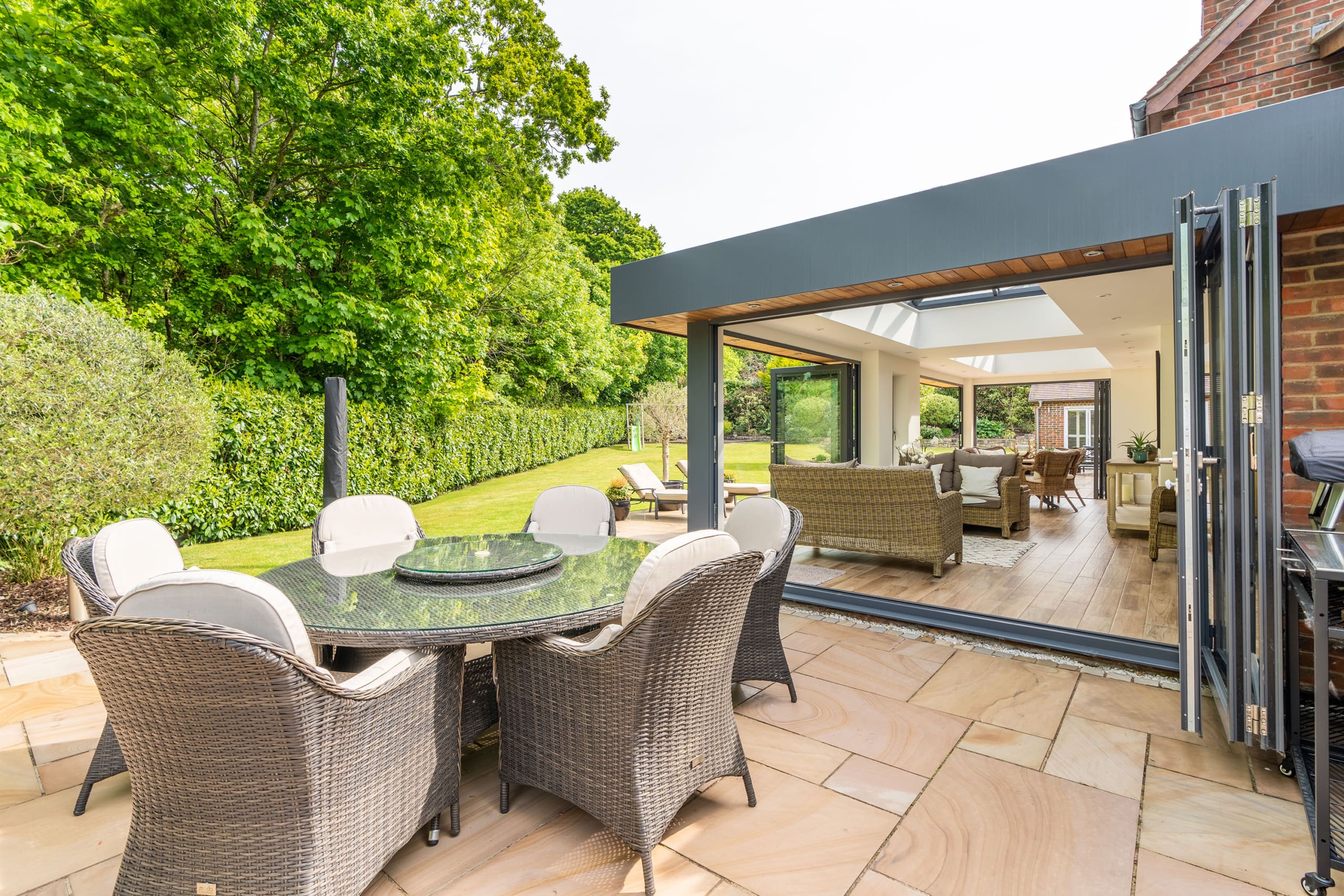View of a orangery extension with bifolding doors and stone slab patio with rattan furniture.