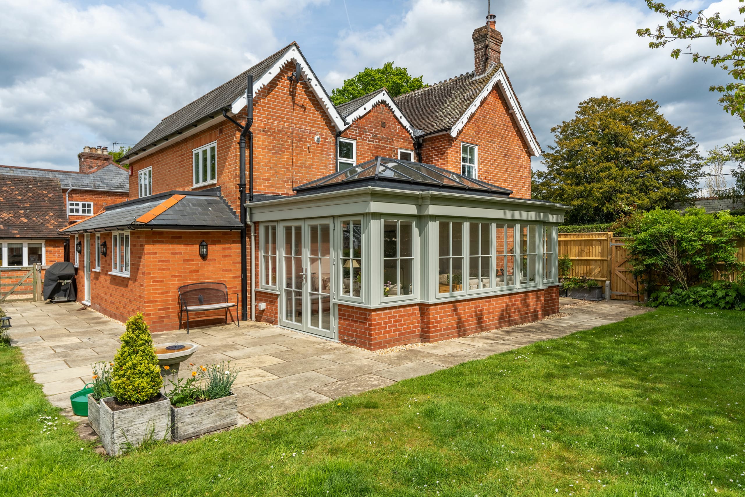 Substantial red brick house with traditional modern orangery extension finished with olive green framing.