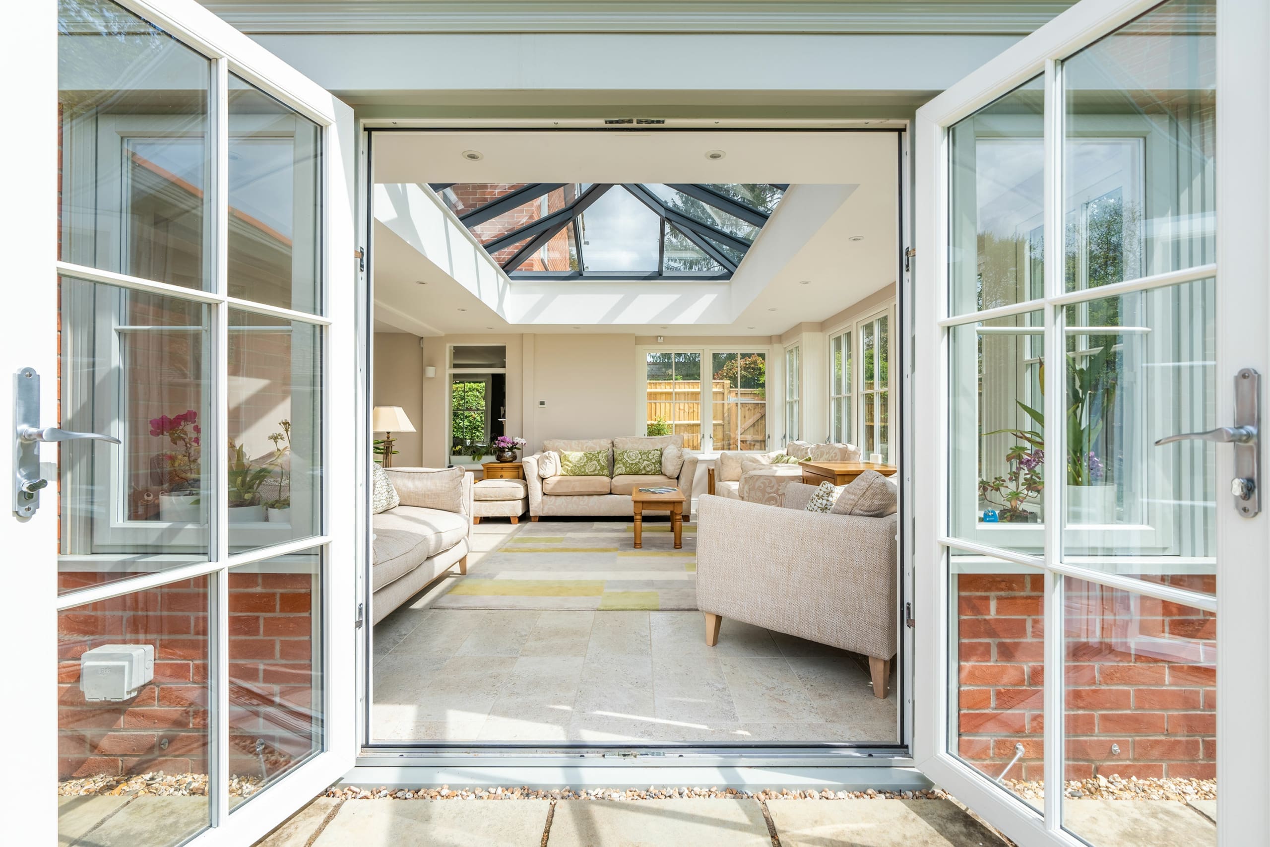 View from the french doors into living room area with comfy sofas, armchairs and oak furnishings, roof lantern and dual aspect windows.