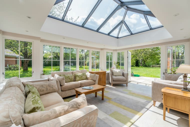 Living room area with comfy sofas, armchairs and oak furnishings, roof lantern and dual aspect windows.