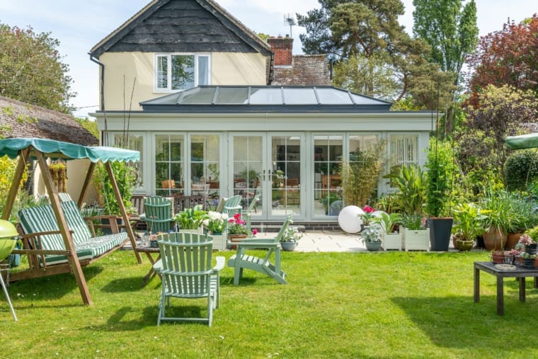 Exterior of a stunning orangery extension finished with green framework and garden furniture.