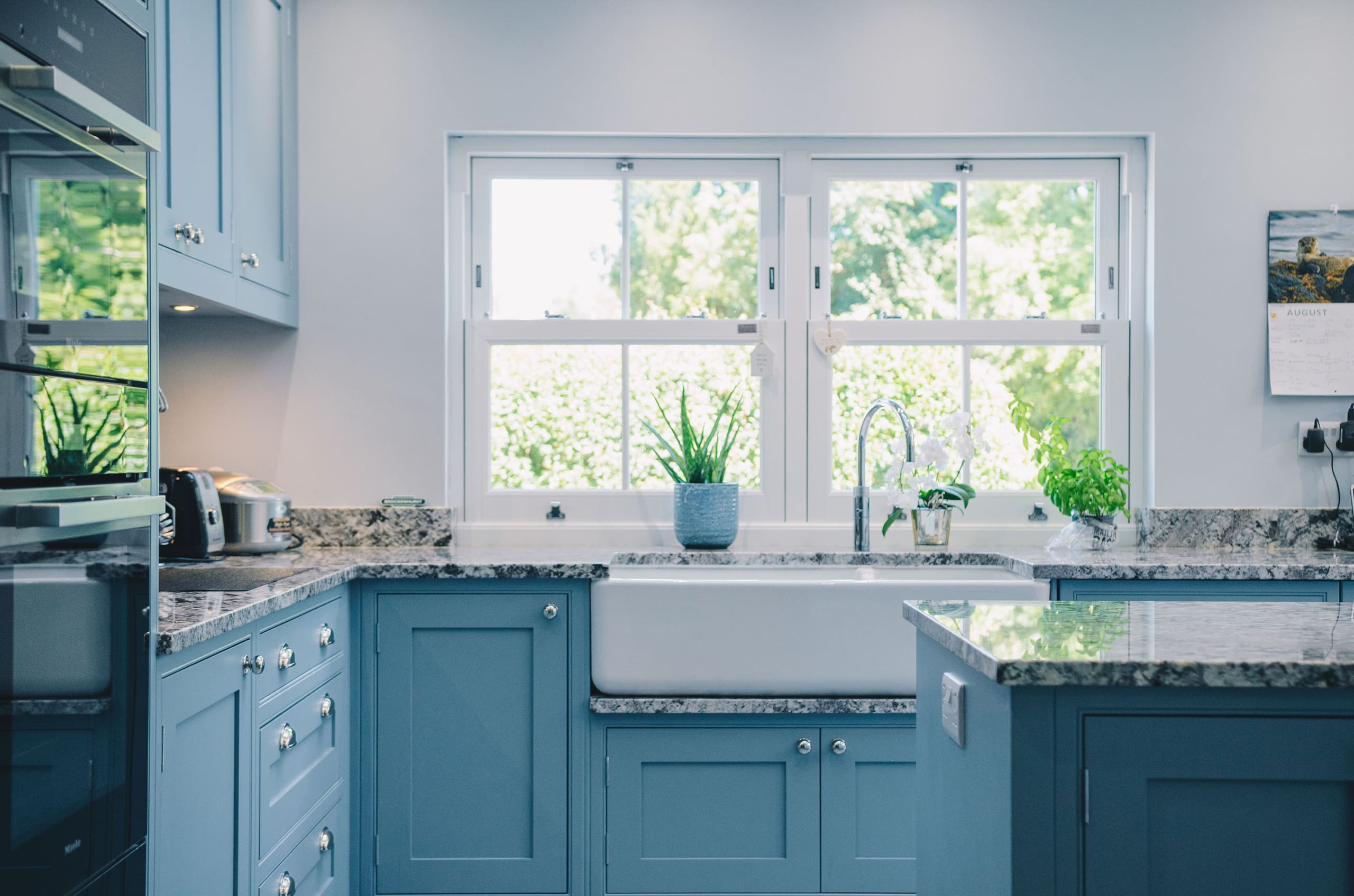 Interior kitchen with blue cupboard fronts and sash window by Master frame.