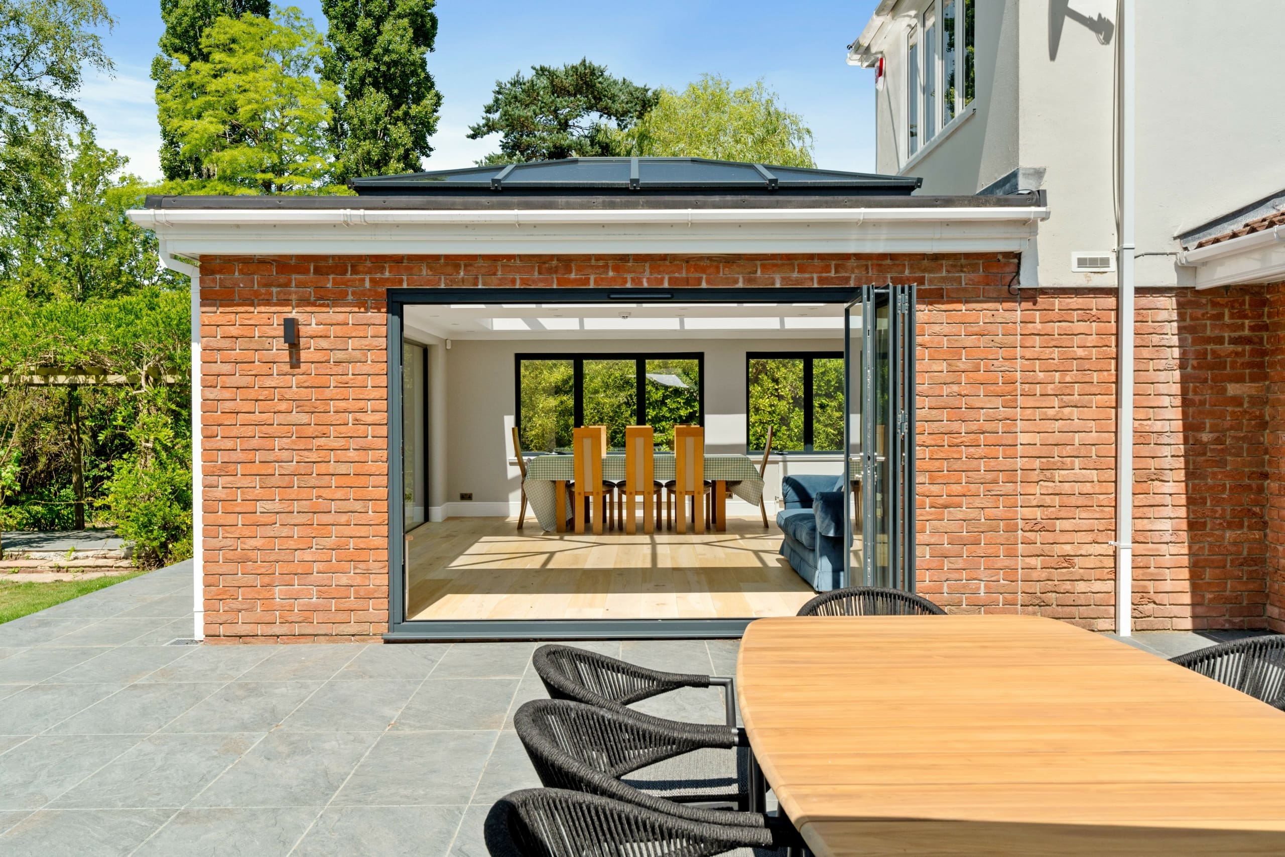 Beautiful modern home with rear bi-folding door on a bright sunny day with partial view of the garden and patio area.