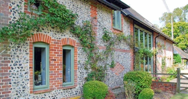Beautiful brick and flint cottage with olive green frames to the windows.
