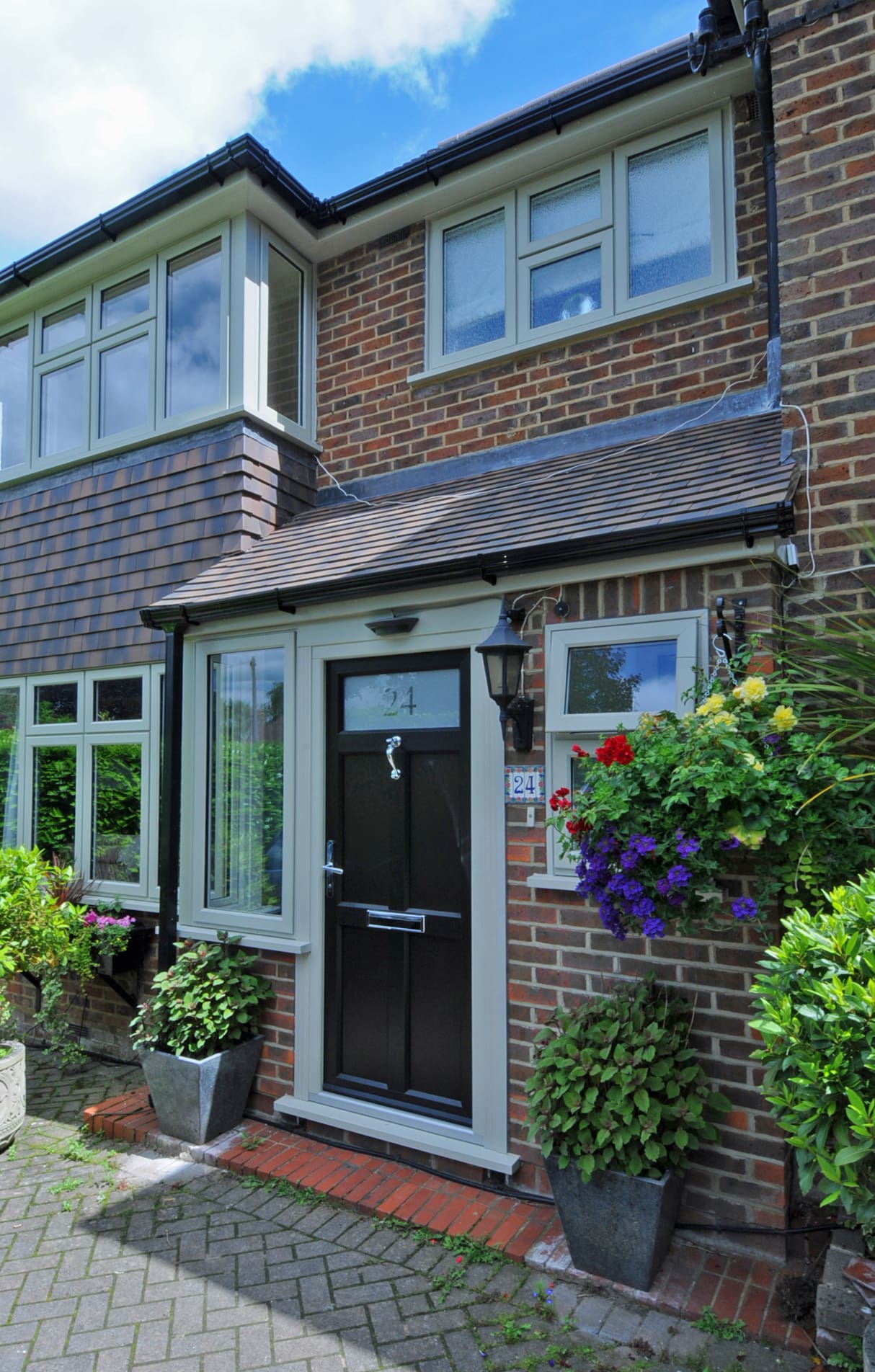 Front of a substantial property with traditional wooden black door and established plants.