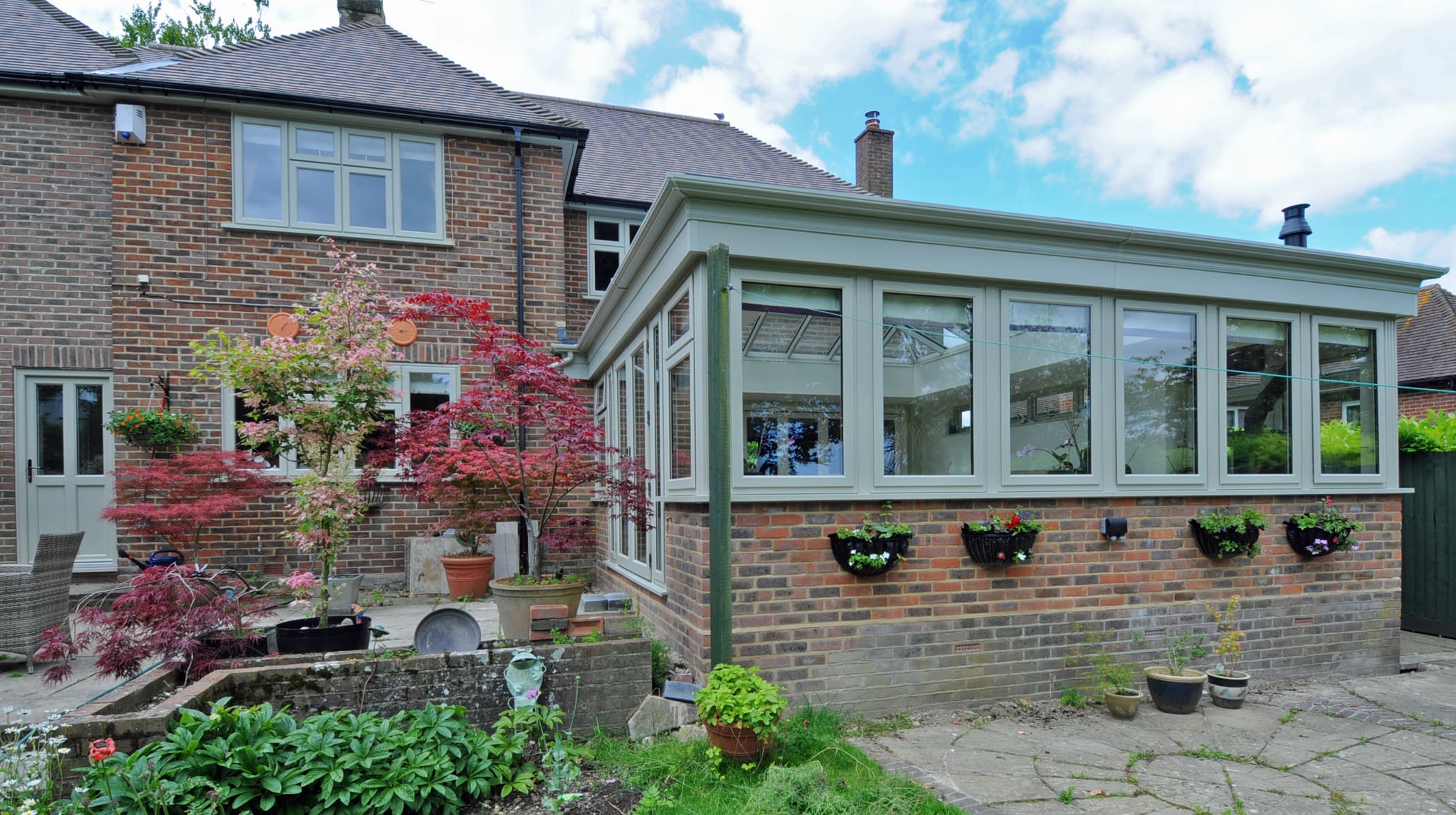 Exterior view of a kitchen extension featuring bespoke glazing with olive green frames.