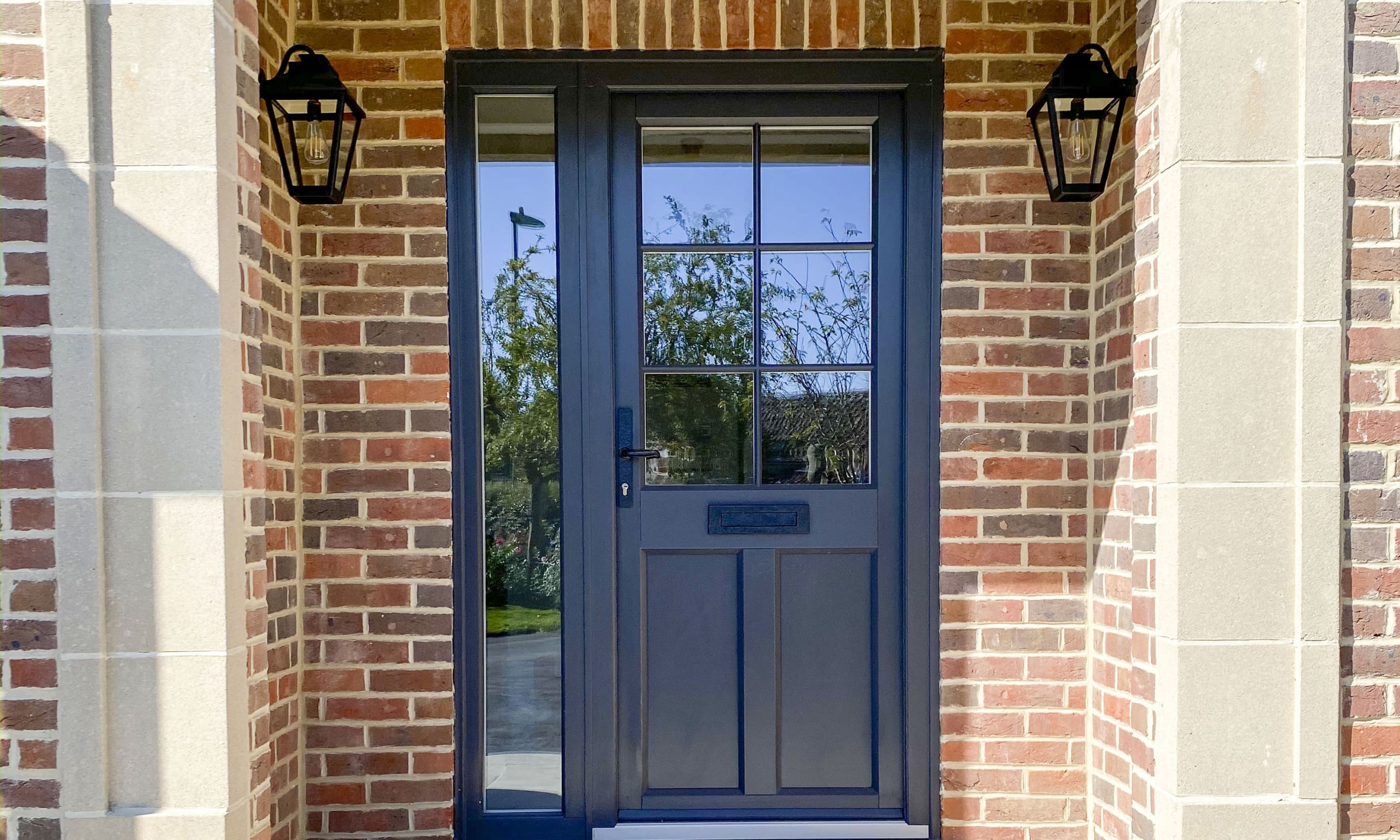 Traditional front door in dark grey with black fixings and a red brick surrounded entrance porch.