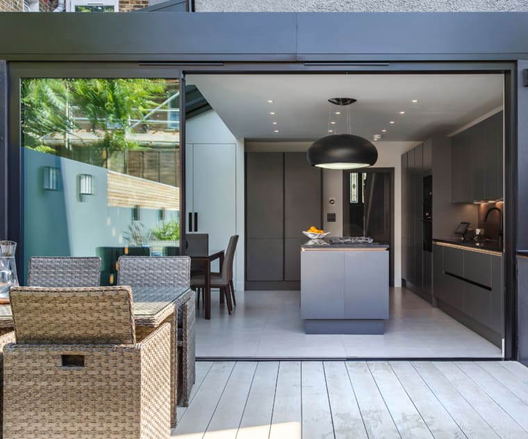 Modern kitchen with decked patio in the foreground and sliding doors seperating the two areas.