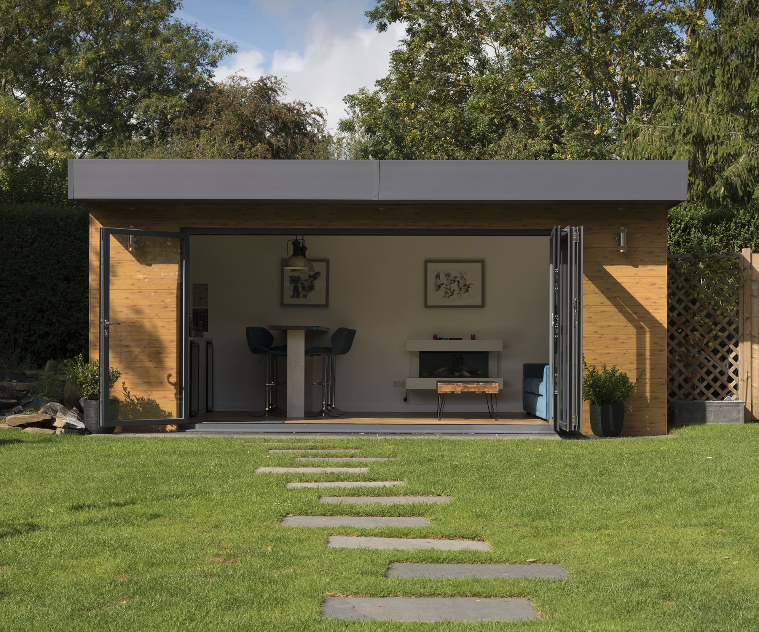Garden office area with open bi-folding doors with timber frame surround and flat roof.