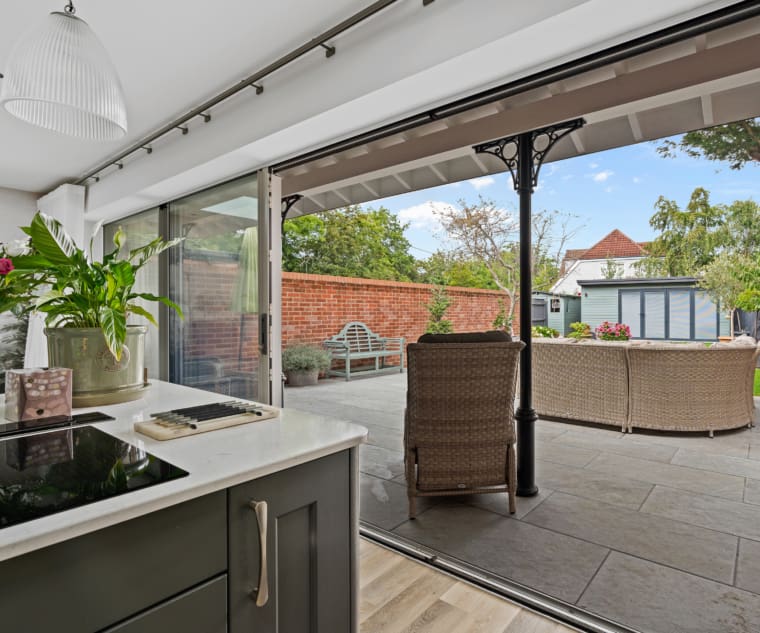 Kitchen extension with sliding doors and view to garden with rattan furniture on a stone patio.