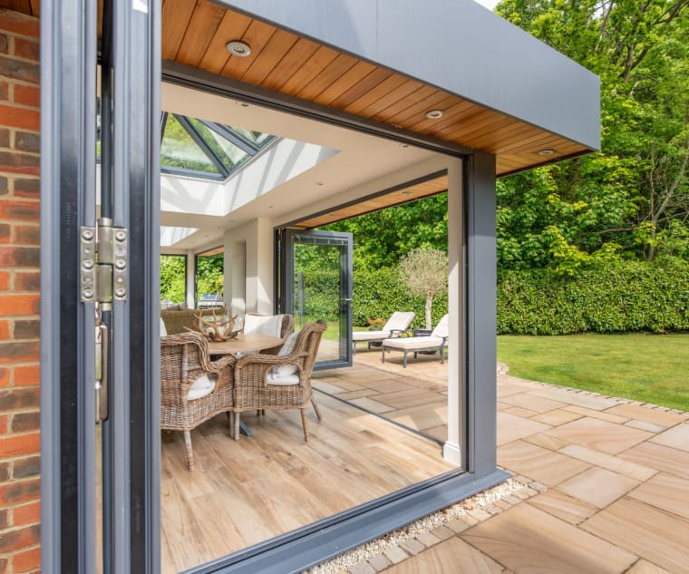 Modern orangery with bi-folding doors and patio area with sun loungers and rattan dining area.