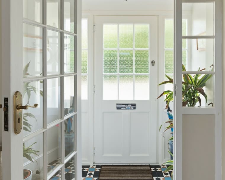 Beautiful entrance doorway with patterned floor tiles and painted wood surround with glass panelled doors.