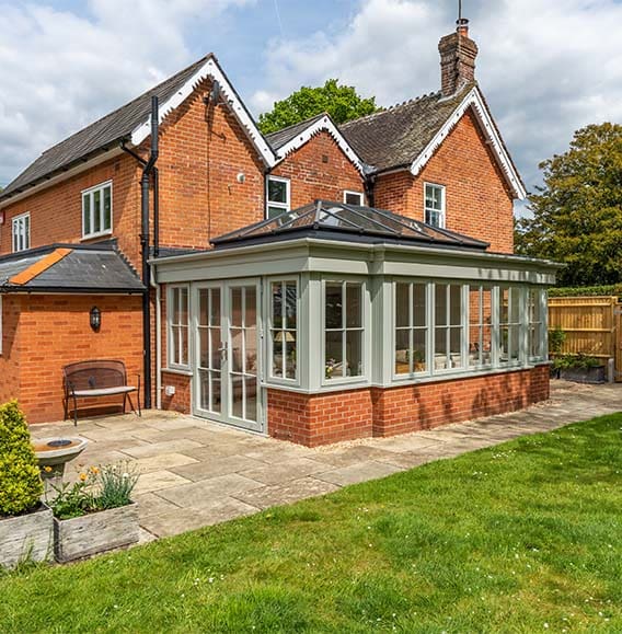 Stunning orangery with olive coloured framework to substantial red brick home.